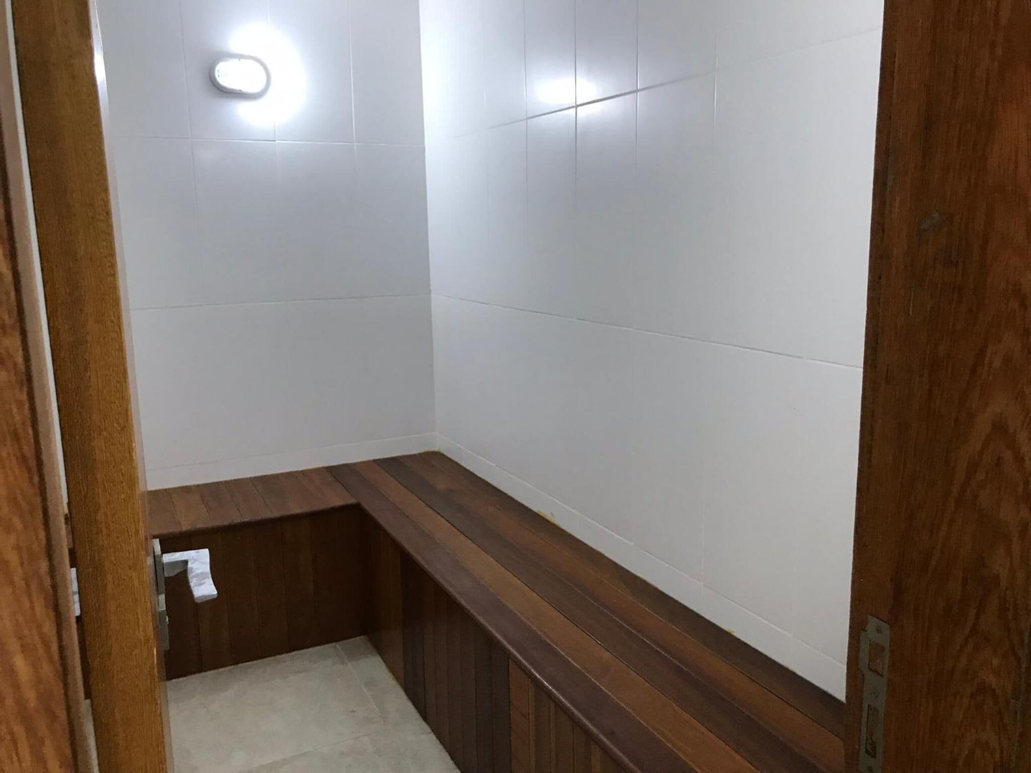 A small, narrow bathroom with white tiled walls and a wooden bench.
