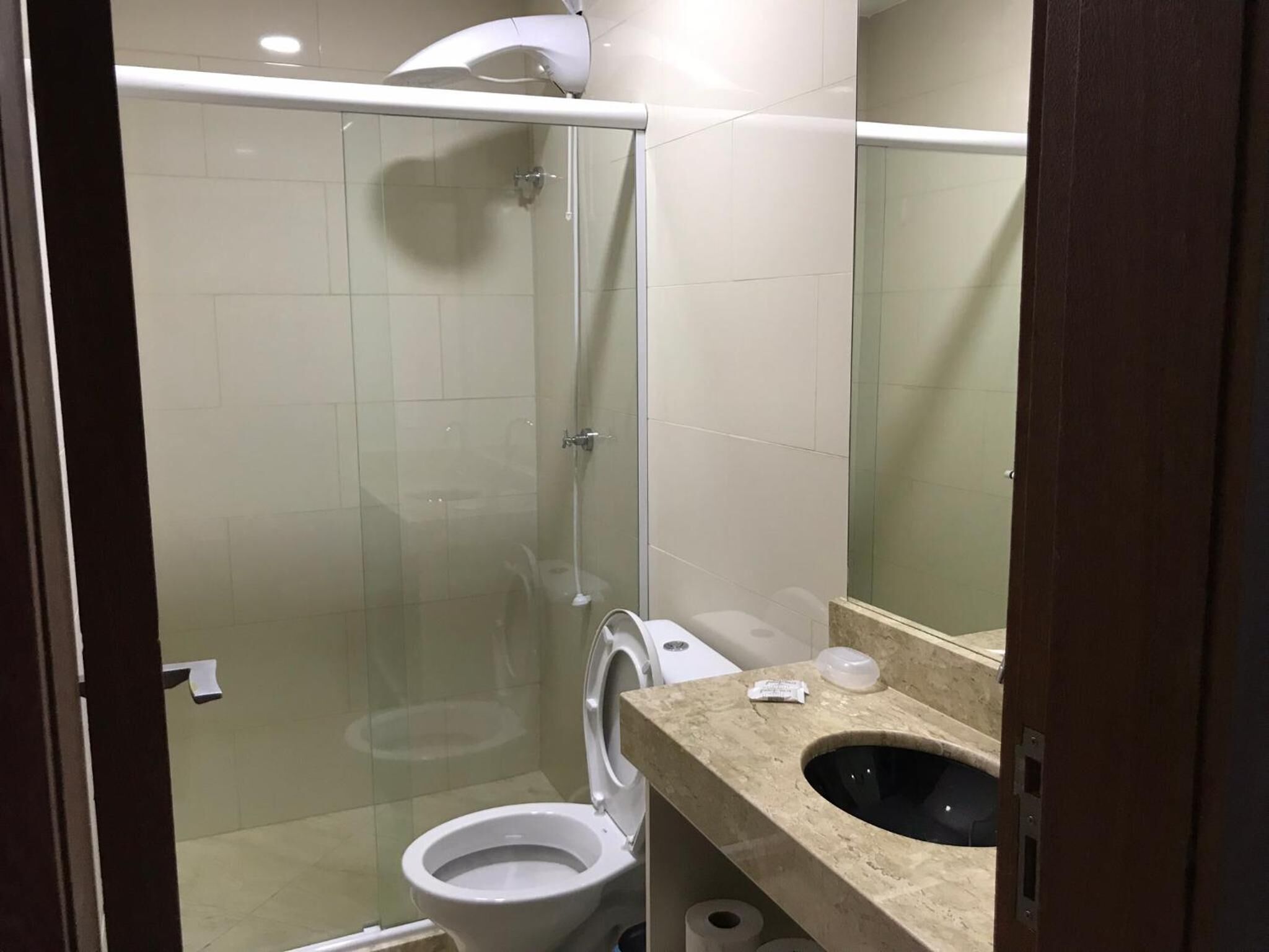 Un baño con ducha de mampara de vidrio, inodoro y lavamanos con espejo.