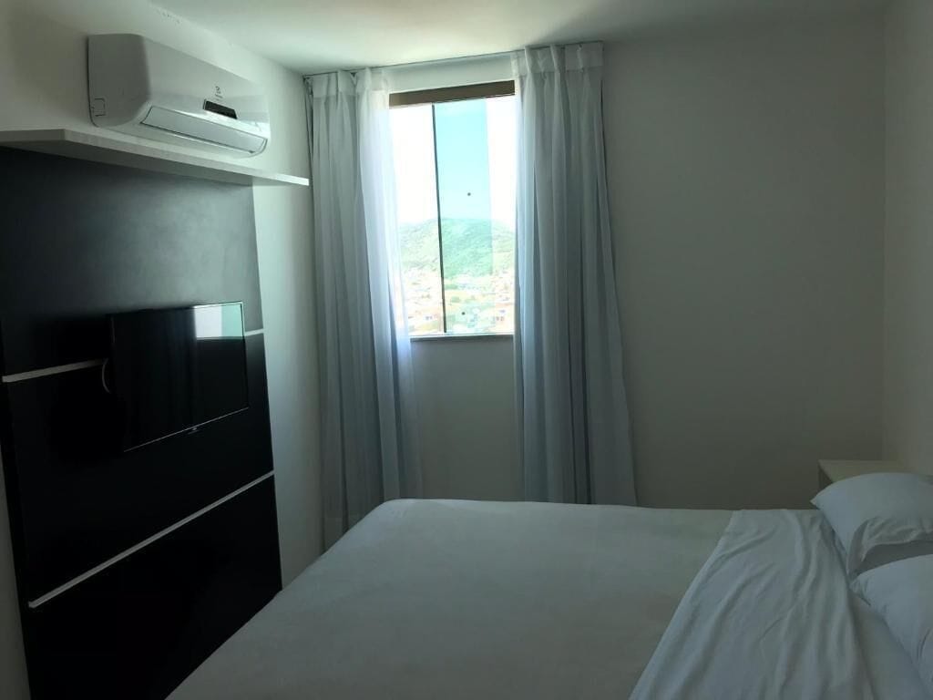 A hotel room with a bed, a TV, and an air conditioning unit.