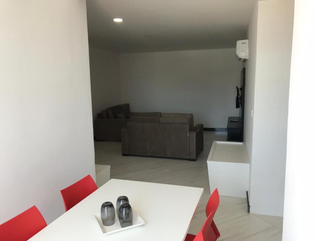 Una sala de estar moderna con un juego de sofá, una mesa de comedor con sillas rojas y una mesa de centro blanca.