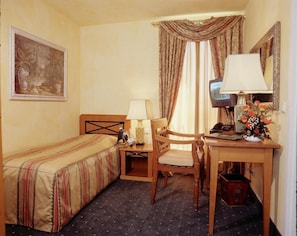 A hotel room with a single bed, a desk with a chair, a telephone, a lamp, and a painting on the wall. - Alter Speicher Hotel & Restaurant (Greifswald)