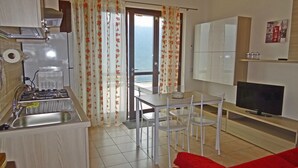 A modern kitchen with a gas stove, sink, and a dining area with white chairs and a table. - La Quiete 29 Holideal (Tremosine)