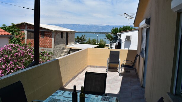 A balcony with a table, chairs, and a bottle of wine. There are buildings and a mountain in the background. - Apartment Vitko (Nin)