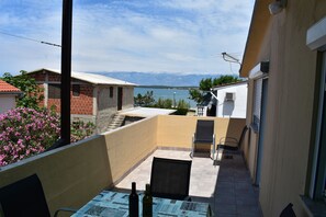 A balcony with a table, chairs, and a bottle of wine. There are buildings and a mountain in the background. - Apartment Vitko (Nin)
