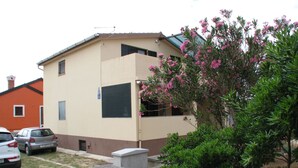 A building with a beige facade, a small window, and a concrete planter with green shrubs. - Apartment Vitko (Nin)