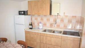 A compact kitchen with wooden cabinets, a built-in microwave, a sink, and a refrigerator. - Apartment Vitko (Nin)