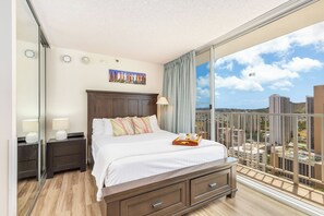 Une chambre moderne avec un grand lit, une table de chevet, une commode et une vue sur le paysage urbain depuis un balcon.