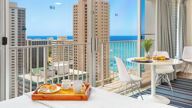A balcony with a dining table, chairs, and a tray with food and drinks. - Ocean-Diamond Head Views Condo at Pacific Monarch Hotel Steps to the Beach (Honolulu)
