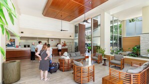 A spacious lobby with wooden furniture, a reception desk, and large windows offering views of the outdoors. - Ocean-Diamond Head Views Condo at Pacific Monarch Hotel Steps to the Beach (Honolulu)