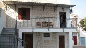 A two-story building with a stone facade, a balcony with wooden furniture, and a staircase leading to the entrance. - Apartment Noa (Kastela)