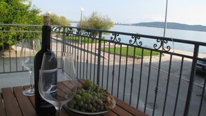 A table with a bottle of wine, a glass, and a plate of grapes, overlooking a waterfront with a metal railing. - Apartment Noa (Kastela)