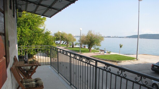A balcony with a table and chairs, overlooking a waterfront with a grassy area and benches. - Apartment Noa (Kastela)