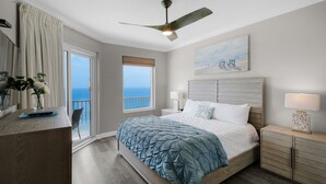 A bedroom with a bed, bedside table, nightstand, and a view of the ocean.