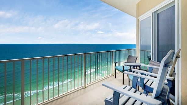 A balcony with a view of the ocean, two chairs, and a table.
