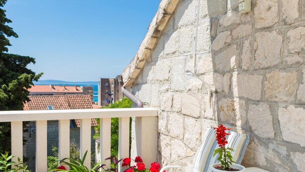 A balcony with potted plants and a table, overlooking a stone wall and buildings. - Split Center Suites (Split)