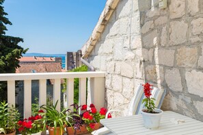 Ein Balkon mit Topfpflanzen und einem Tisch, mit Blick auf eine Steinmauer und Gebäude.