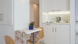 A compact kitchen with white cabinets, a small table with a floral tablecloth, and a chair. - Split Center Suites (Split)