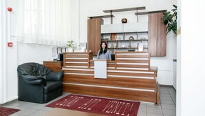 A reception area with a wooden desk, a black leather sofa, and a red rug with text. - HOTEL GLOBAL (Bra?ov)