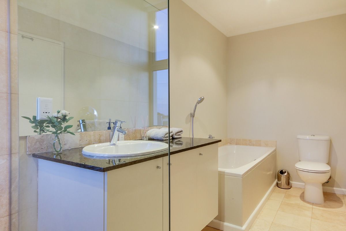 Ein modernes Badezimmer mit einer Glasdusche, einem Waschbecken mit Spiegel, einer Toilette und einer Badewanne.