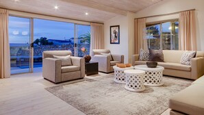 Ein geräumiges Wohnzimmer mit einem großen Schiebeglasfenster, das auf einen Balkon führt, einer beigefarbenen Sofagarnitur, einem Couchtisch und einem gemusterten Teppich.