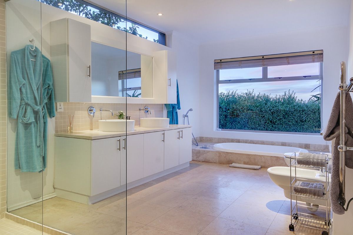 A modern bathroom with a large window, a bathtub, a shower, and a vanity with a mirror.