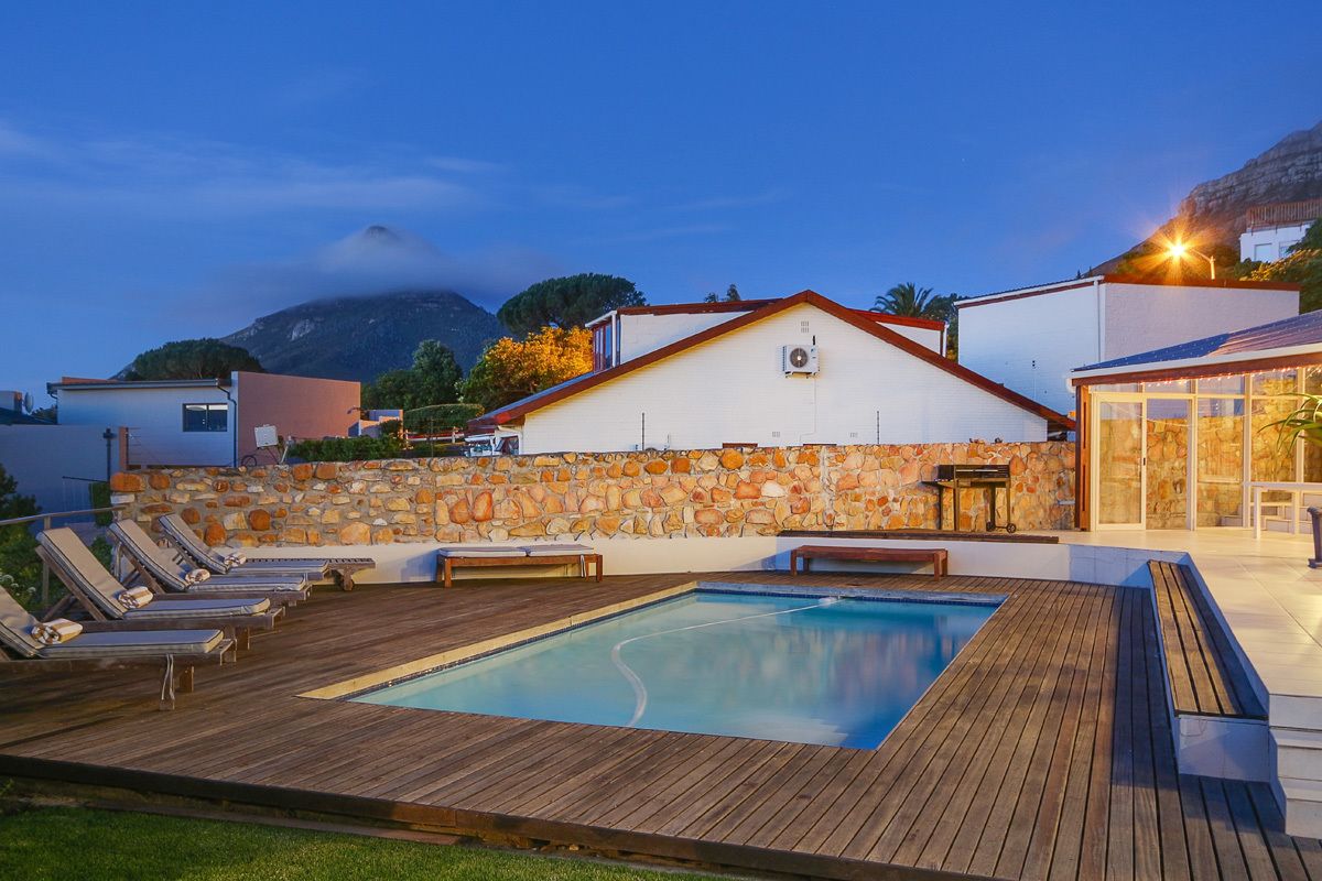 A pool area with lounge chairs, a stone wall, and a building with a red roof.