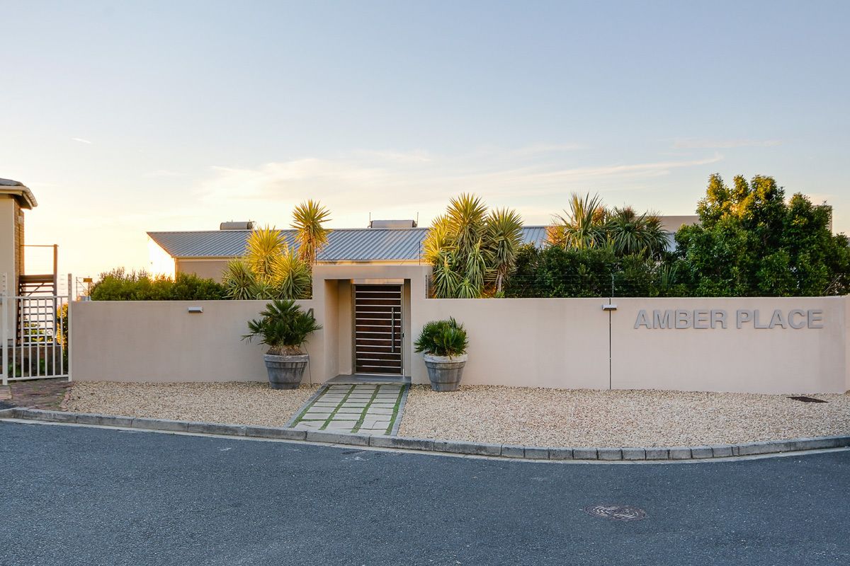 A residential building with a gated entrance, a nameplate reading "AMBER PLACE," and a small garden area with potted plants.