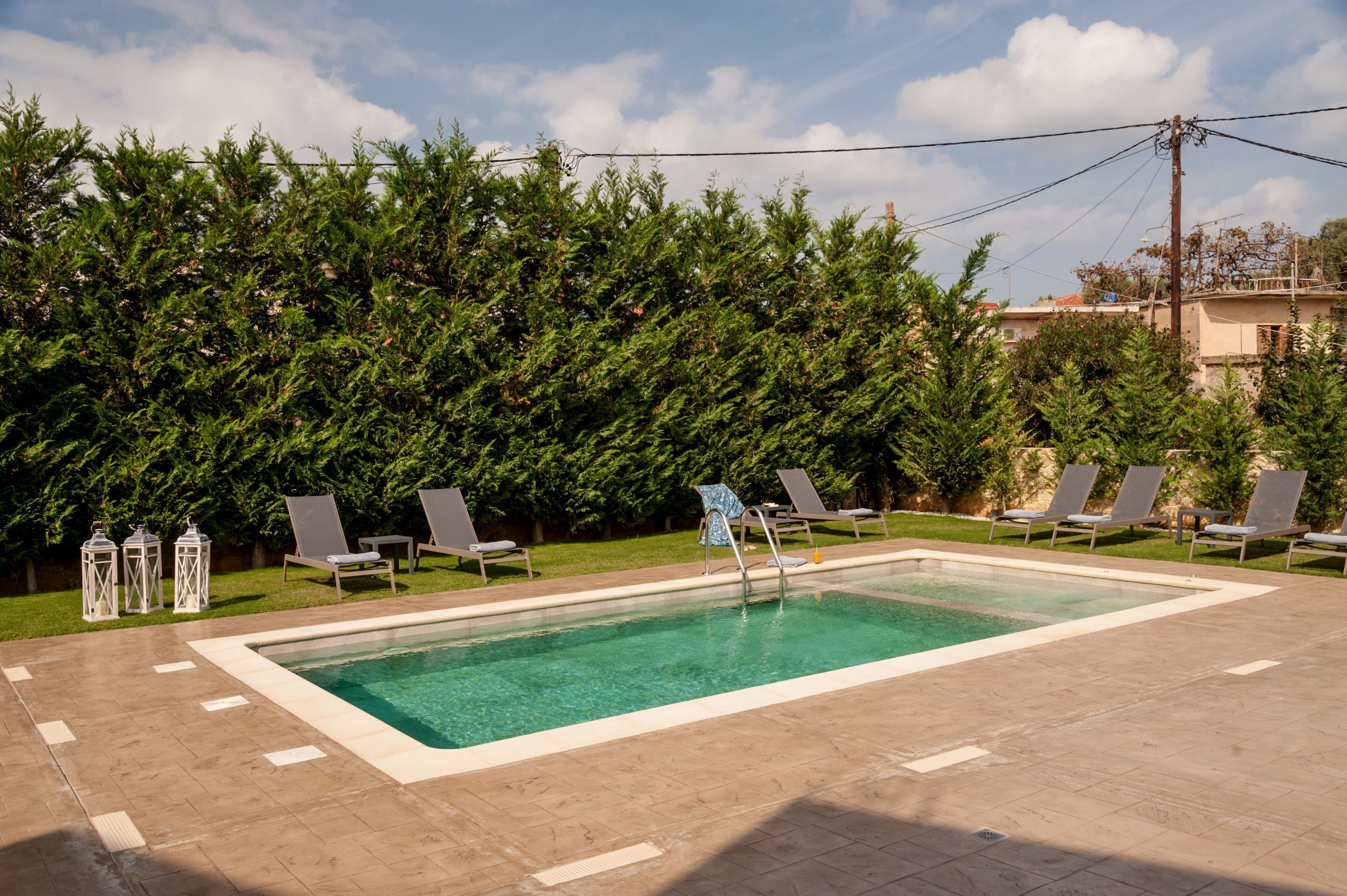 Una piscina rectangular con solárium de baldosas, rodeada de sillones de descanso y faroles blancos.