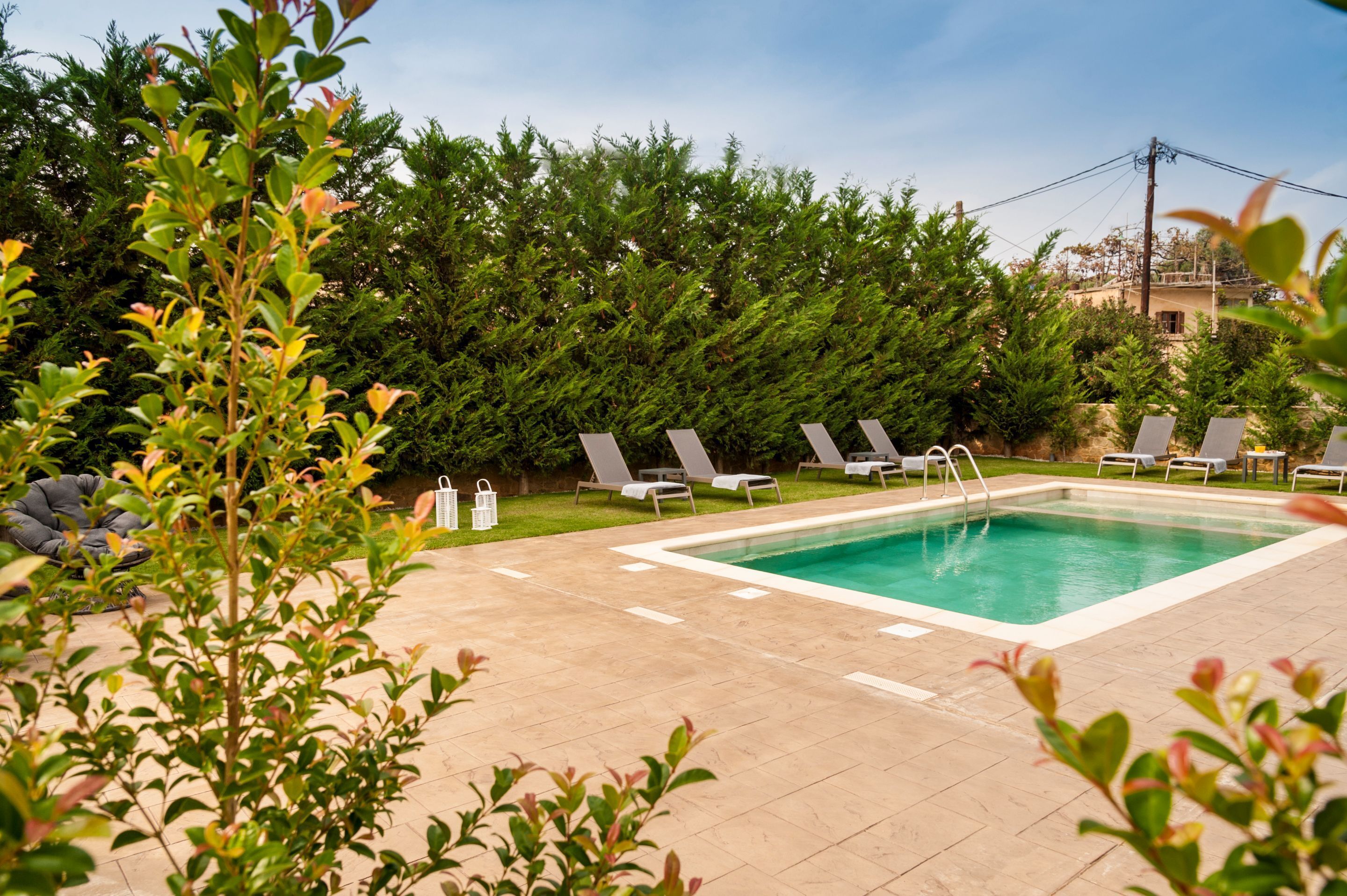 A rectangular pool with a tiled deck, surrounded by lounge chairs and a dense hedge.