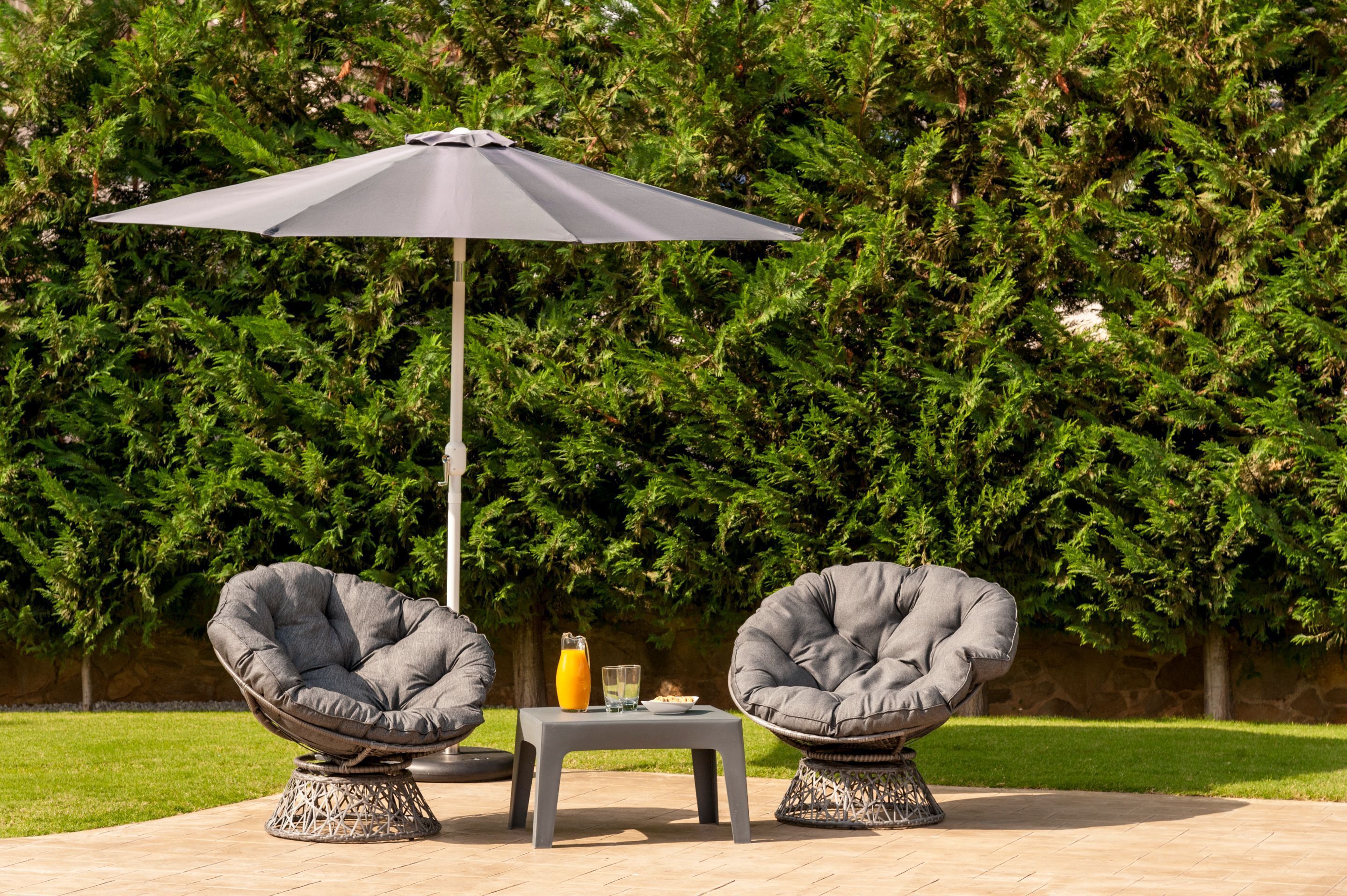 An outdoor seating area with two cushioned chairs, a small table, and a large umbrella.