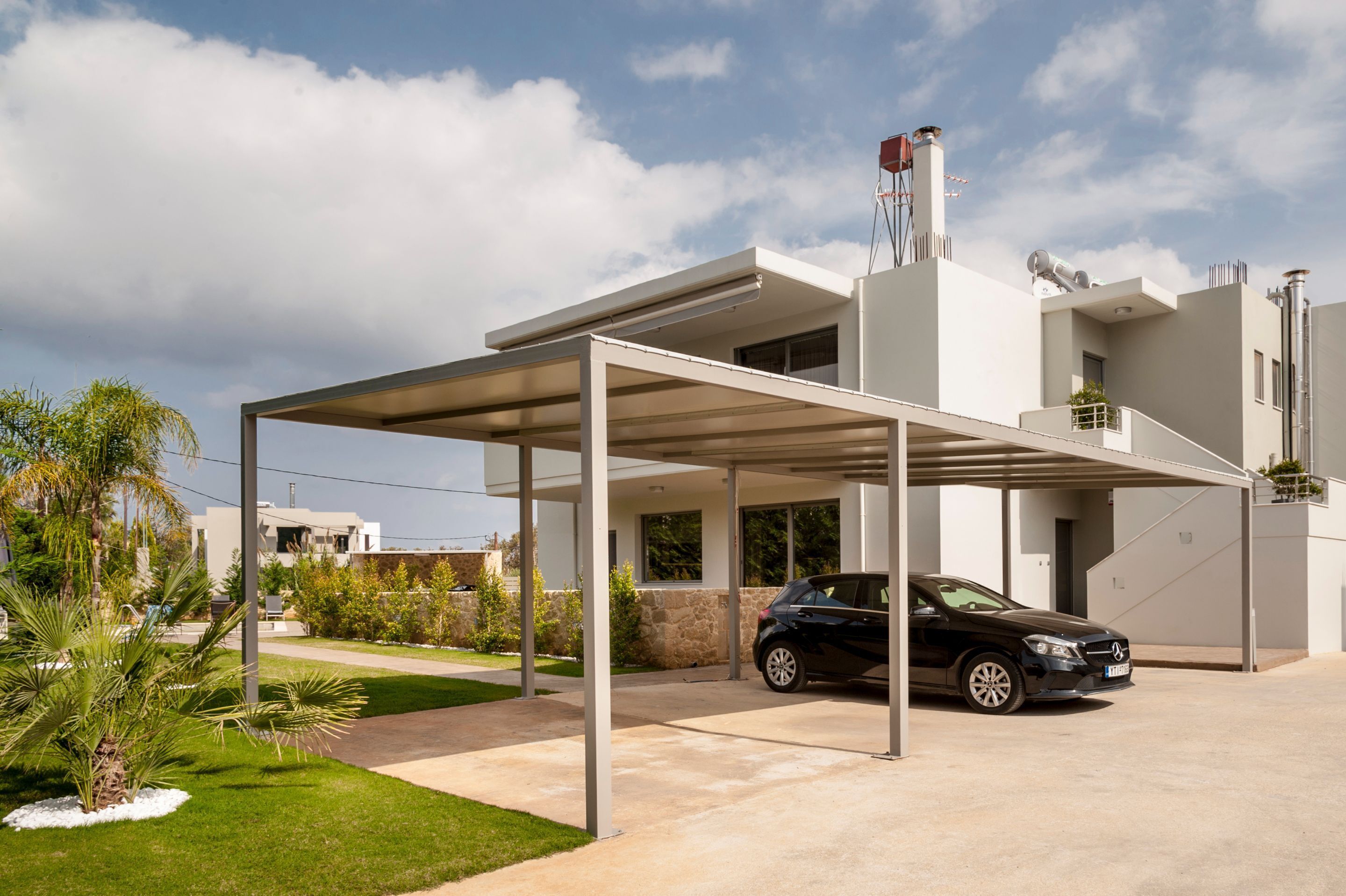 Een modern huis met een overdekte oprit, een zwarte auto geparkeerd en een verzorgd gazon.