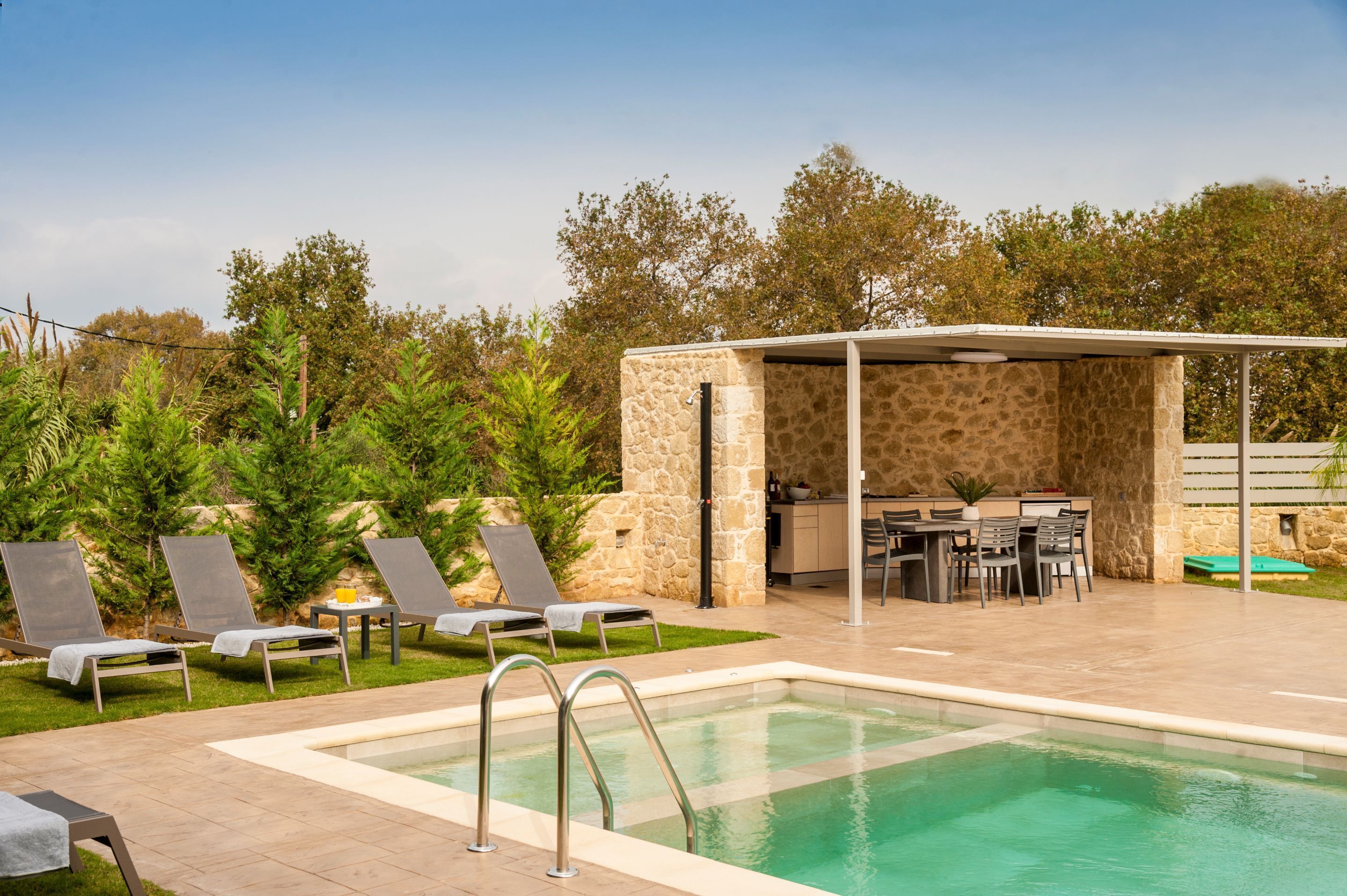 A pool area with lounge chairs, a covered seating area, and a stone wall.