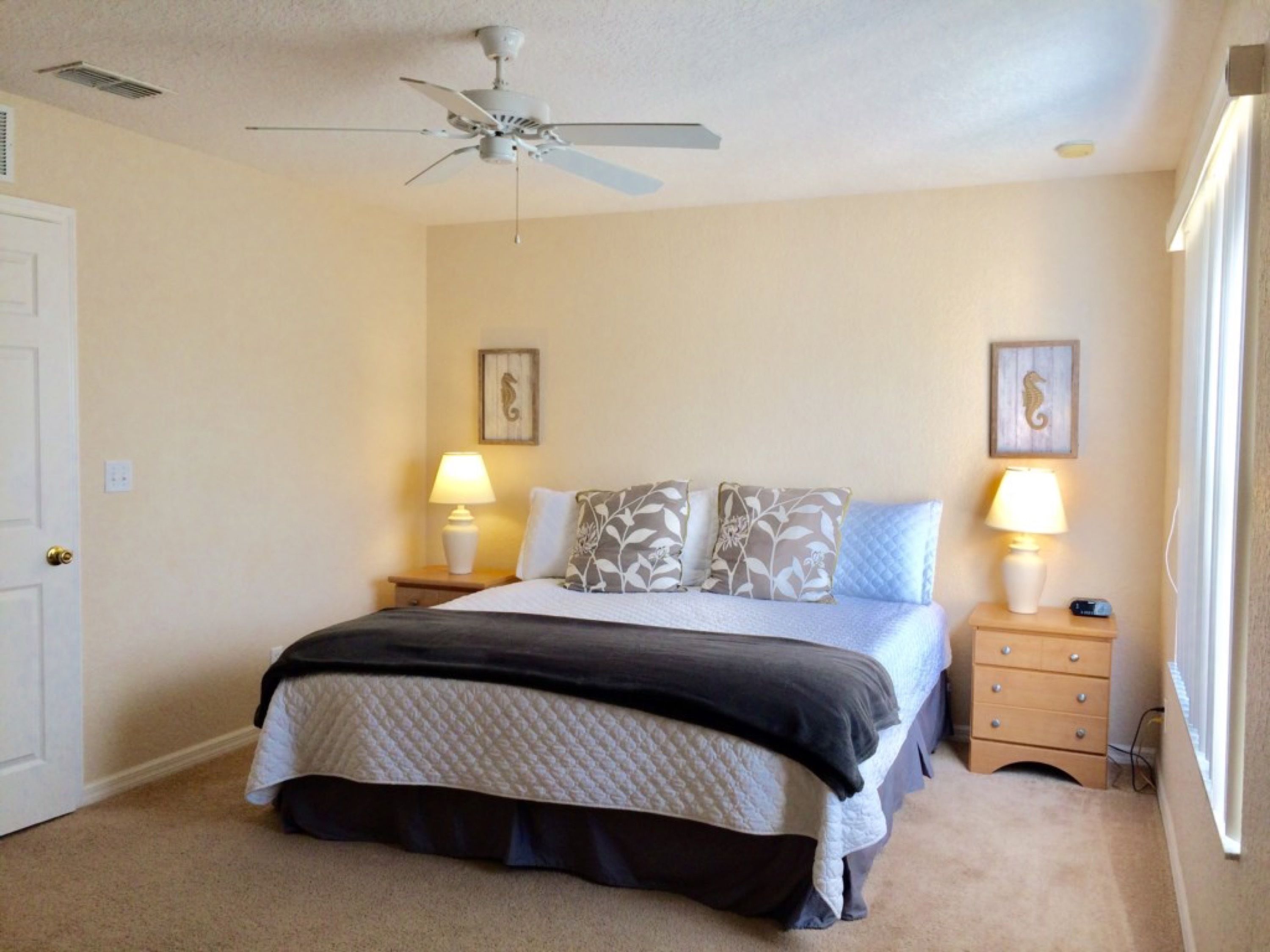 A bedroom with a bed, two bedside tables with lamps, a ceiling fan, and two wall-mounted pictures.