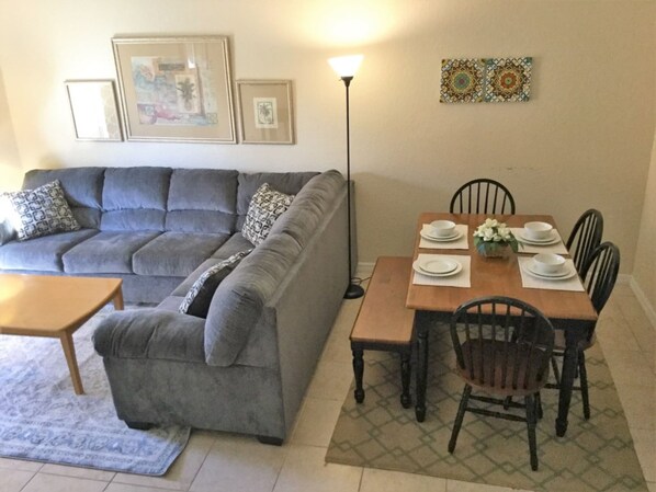 A living room with a grey sofa, a wooden dining table with chairs, and a floor lamp.