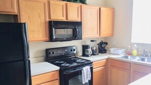 Une cuisine avec des meubles de rangement en bois, un réfrigérateur noir, un four à micro-ondes, une cuisinière et une machine à café.