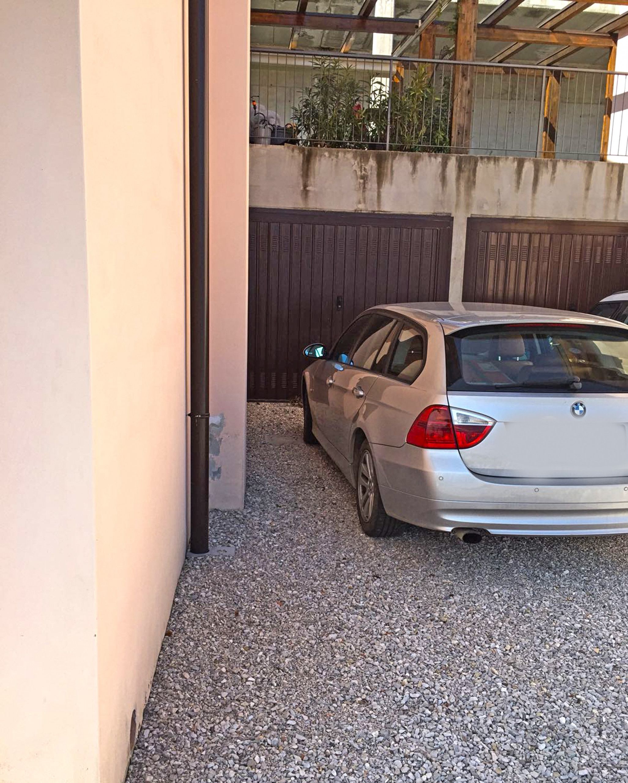 A silver BMW parked in a gravel driveway with a wooden fence and a metal gate in the background.