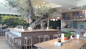 A restaurant with a central bar area, multiple seating options including bar stools and tables, and a large tree in the middle. - Les Villages Nature Paris (Villeneuve-le-Comte)