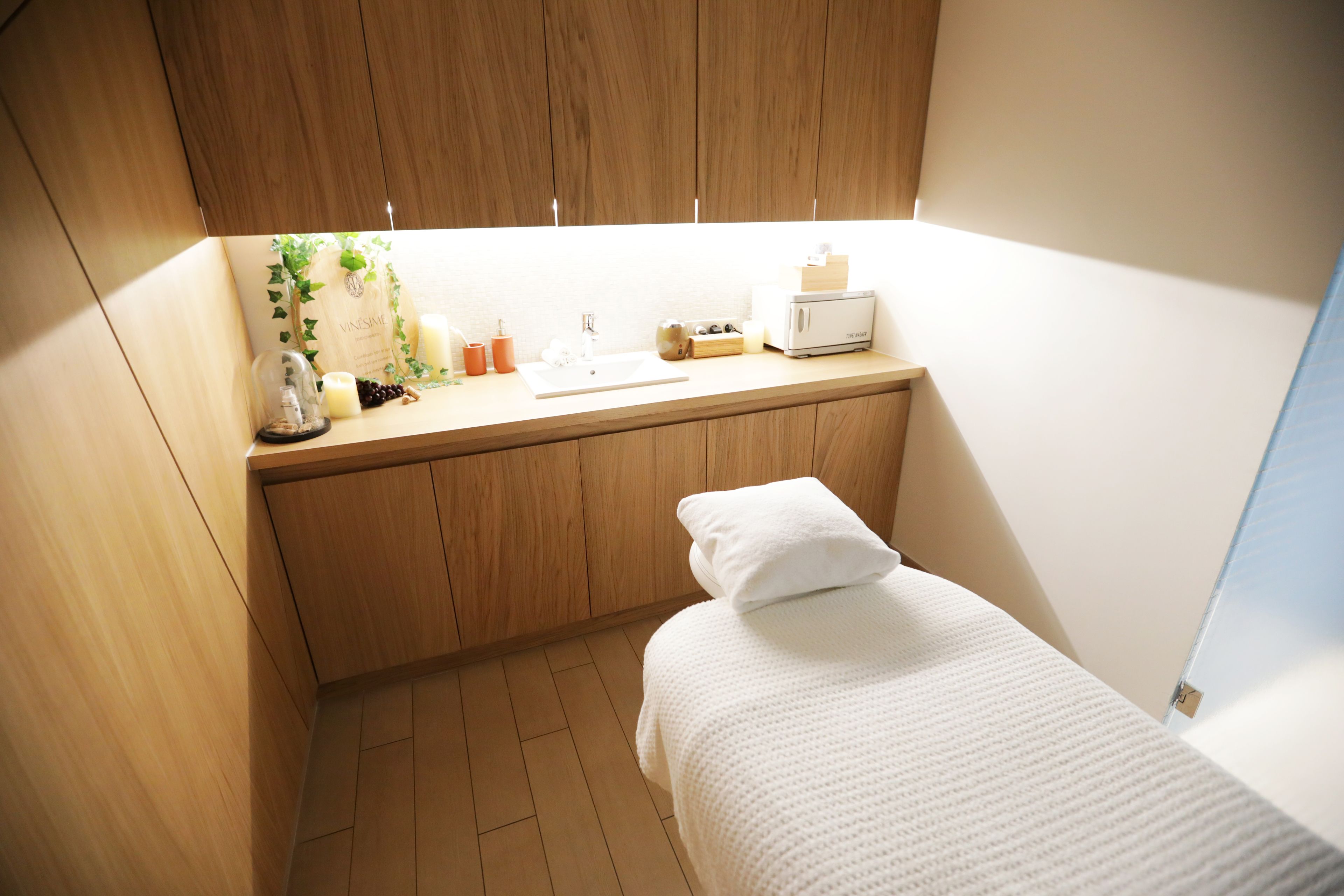 A compact room with a wooden cabinet, a small sink, a bed with a white pillow, and a window.