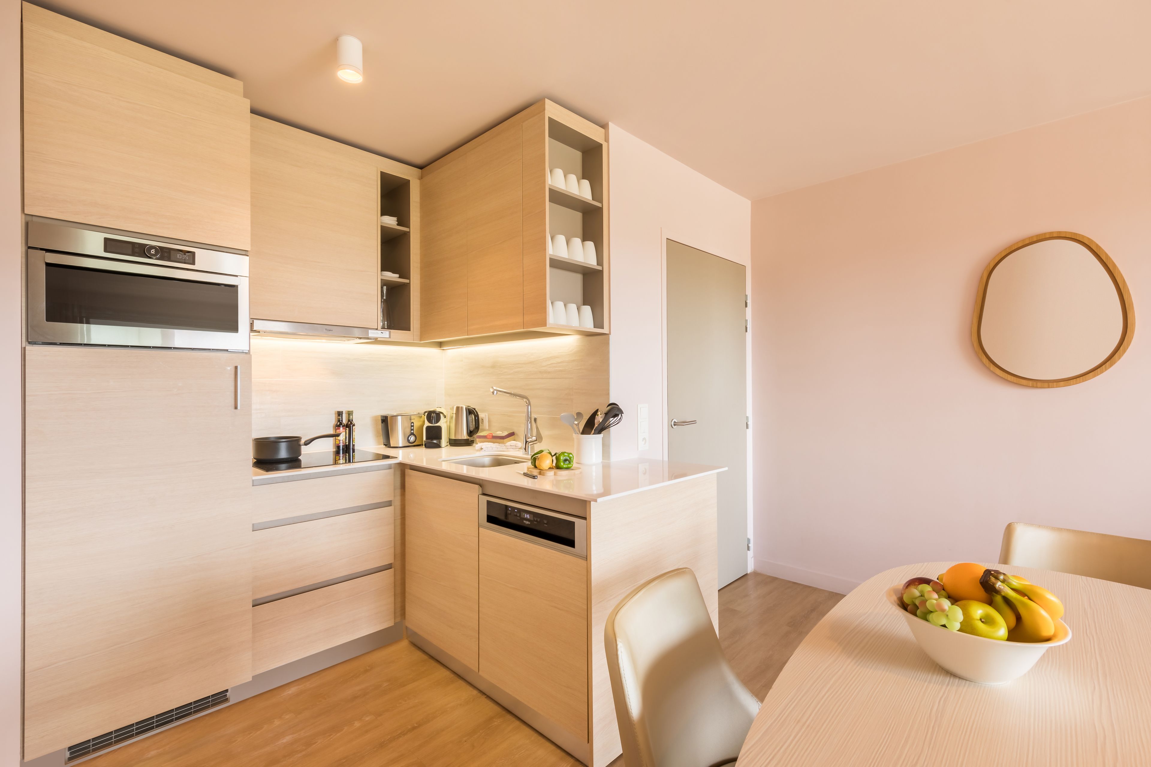 A modern kitchen with built-in appliances, a dishwasher, and a dining area with a bowl of fruit.