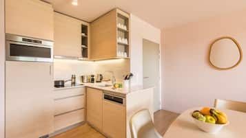 A modern kitchen with built-in appliances, a dishwasher, and a dining area with a bowl of fruit.