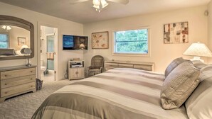 Makuuhuone, jossa on sänky, kattotuuletin, televisio, ikkuna ja taideteoksia seinillä.