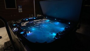 A hot tub with illuminated jets, set in a wooden cabin with a window and a sign on the wall. - Centennial Cabin w/ Hot Tub, Sauna & Pool Table! (Centennial)