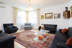 Un soggiorno con un divano in pelle nera, un tavolino in vetro, un tappeto decorato e un lampadario.