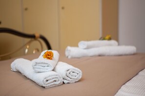 Un letto rifatto con asciugamani bianchi arrotolati e un asciugamano con un fiore giallo.