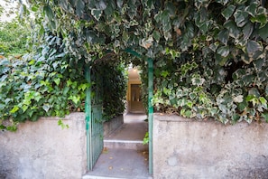 Un vialetto stretto in cemento che conduce attraverso un cancello in metallo verde, circondato da fitta vegetazione.