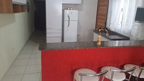 Une cuisine avec un réfrigérateur blanc, un plan de travail rouge et un petit îlot central doté de chaises.
