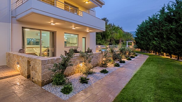 A modern two-story house with a stone facade, a balcony, and a well-maintained garden with a pathway. - Kagiemar Luxury House (Chania)
