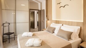 A modern hotel room with a large bed, a wooden headboard, and a view of the hallway. - Kagiemar Luxury House (Chania)