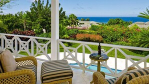 A covered outdoor area with wicker furniture and a pool, overlooking a lush landscape and the ocean. - Villa Oceana (Holetown)