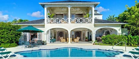A two-story house with a swimming pool, outdoor seating, and a balcony.